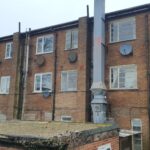 A brick building with several satellite dishes on the roof and loft ladders.