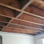 A room with a wooden ceiling and a sink, featuring loft boarding.