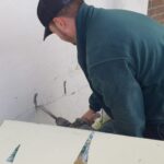 A man is repairing a wall with a screwdriver in his loft.