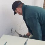 A man is working on a wall in front of a house, using loft insulation installers.