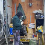 A man in a hoodie is opening the back of a truck to unload some items.