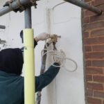 A man is working on a brick wall with a pipe, possibly installing loft boarding.