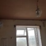 An unfinished kitchen with a window and a fan that needs loft insulation.