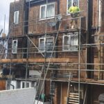 A man is working on a building with scaffolding, installing loft insulation.