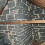 An attic with a brick wall and wooden beams that has been insulated with loft insulation.