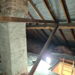 An attic with a light, a brick wall, and loft insulation.