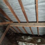An attic with insulation and wooden beams, equipped with loft insulation installers.