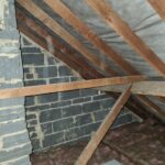 An attic with wooden beams and insulation, perfect for loft hatches or loft insulation installers.