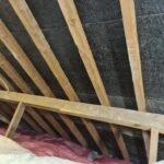 An attic with wooden beams and loft insulation.