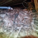 Insulation material and an air duct in an attic, showing a poorly maintained area with visible wear and damage.