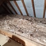 Insulation material spread out between wooden beams in an attic, with dim lighting.