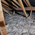 Interior of an attic showing wooden beams and insulation material spread across the floor.