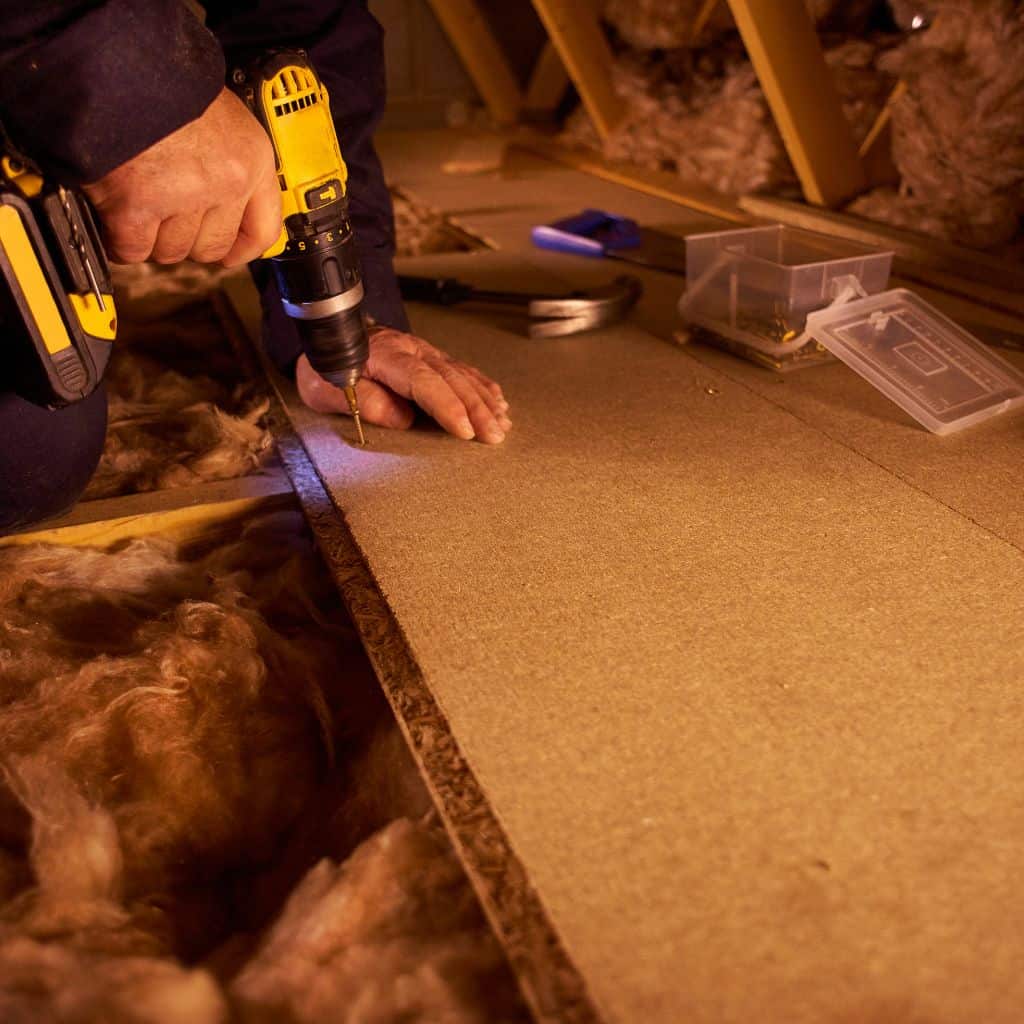 Loft insulation being installed by a professional with a drill in an attic space.