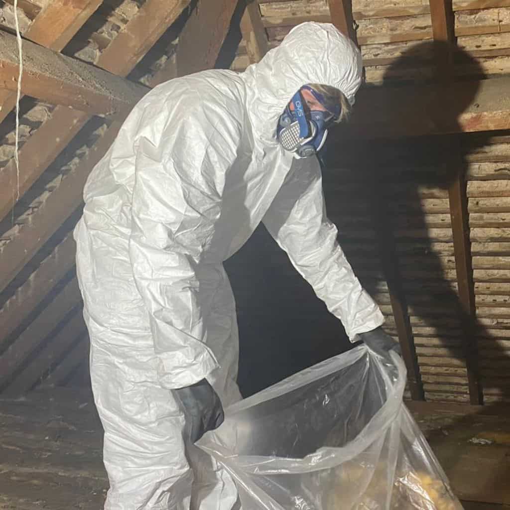 Worker in protective gear installing loft insulation in an attic.