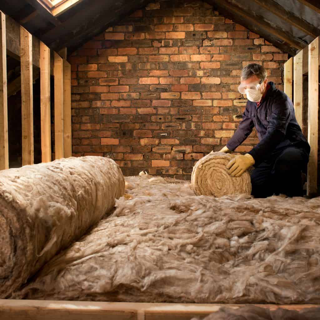 Installer fitting loft insulation between roof rafters in attic space.