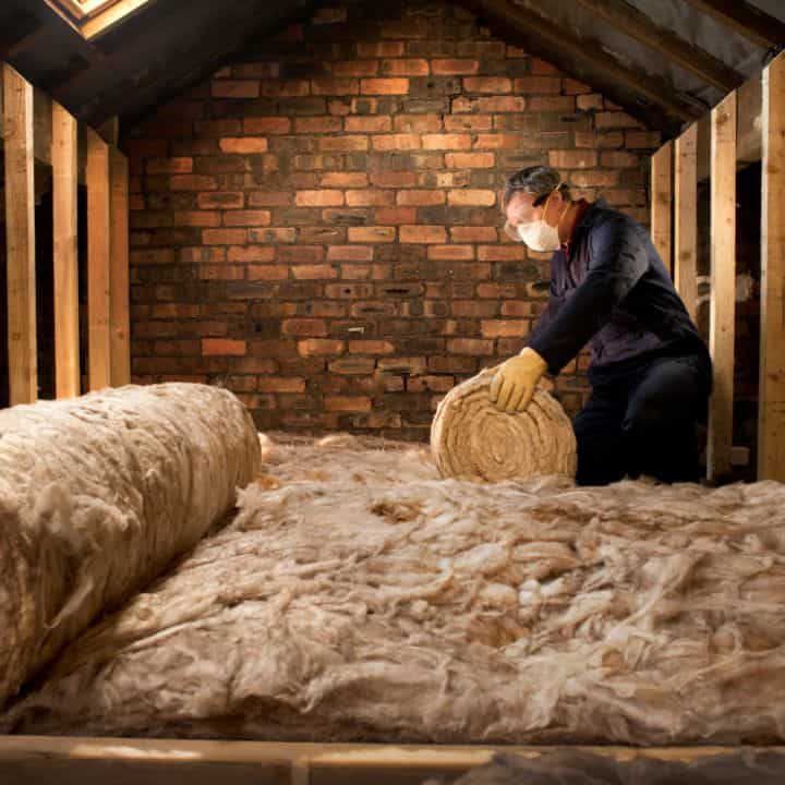 Installer fitting loft insulation between roof rafters in an attic.
