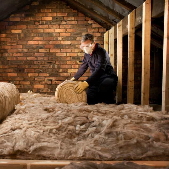 Installer fitting loft insulation between wooden beams in an attic space.