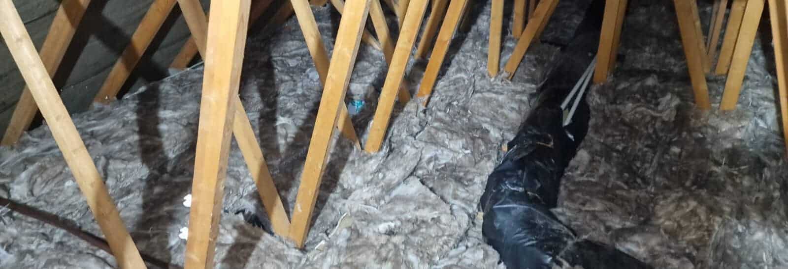 Insulation being installed under floorboards in a loft space.