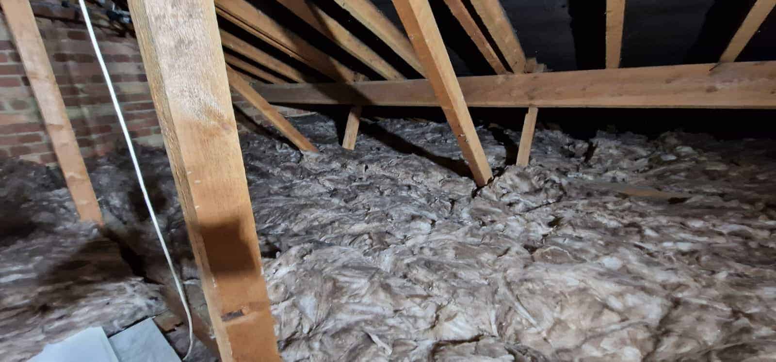 Insulation being installed in a loft space with wooden beams and insulation material.
