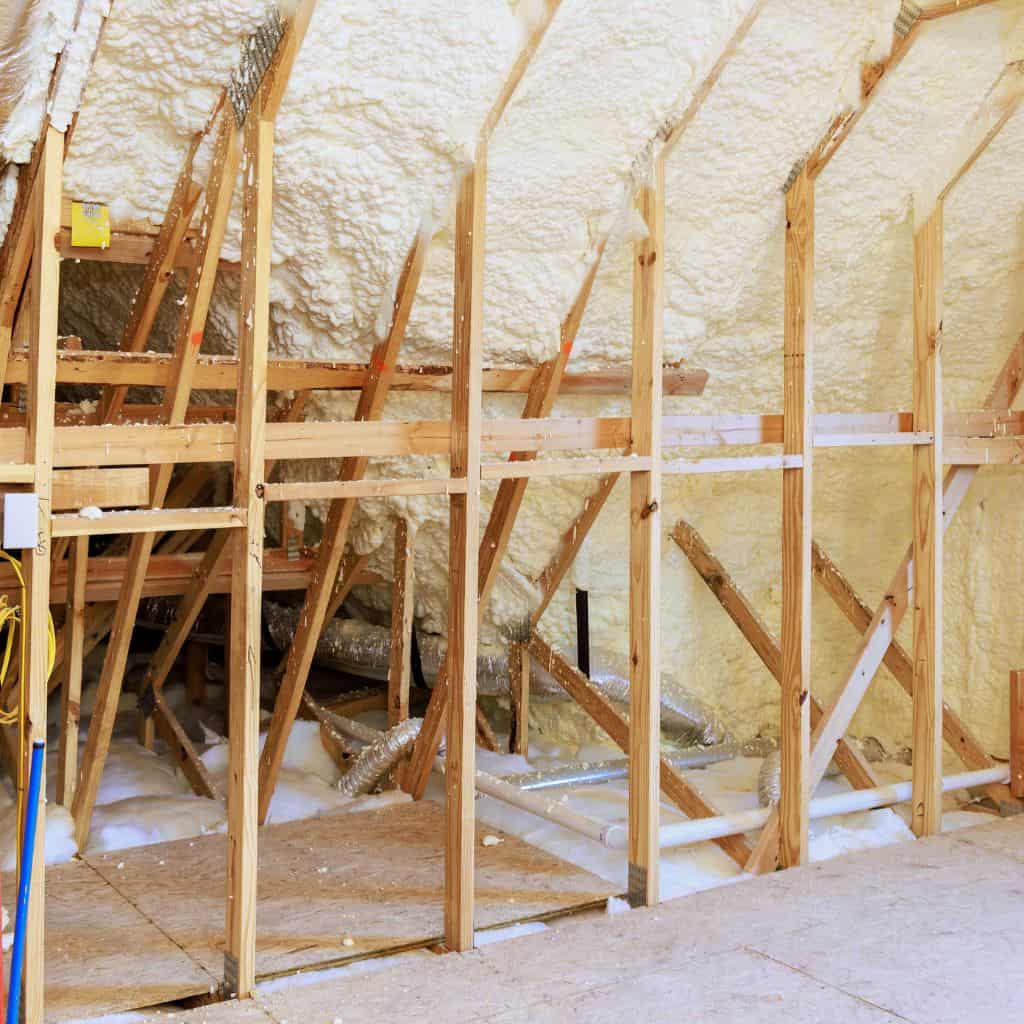 Loft insulation specialists removing spray foam insulation in attic space.