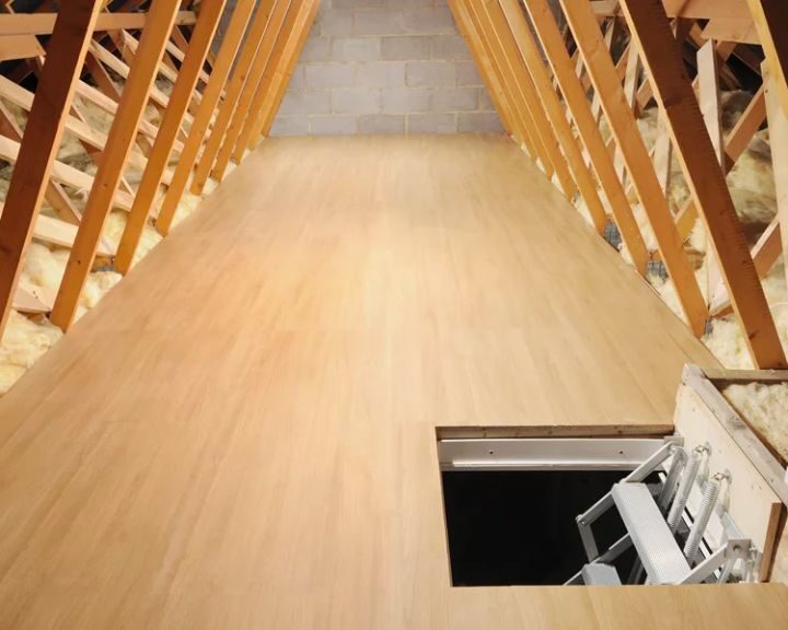 An attic with a wooden floor and a door, equipped with loft ladders.