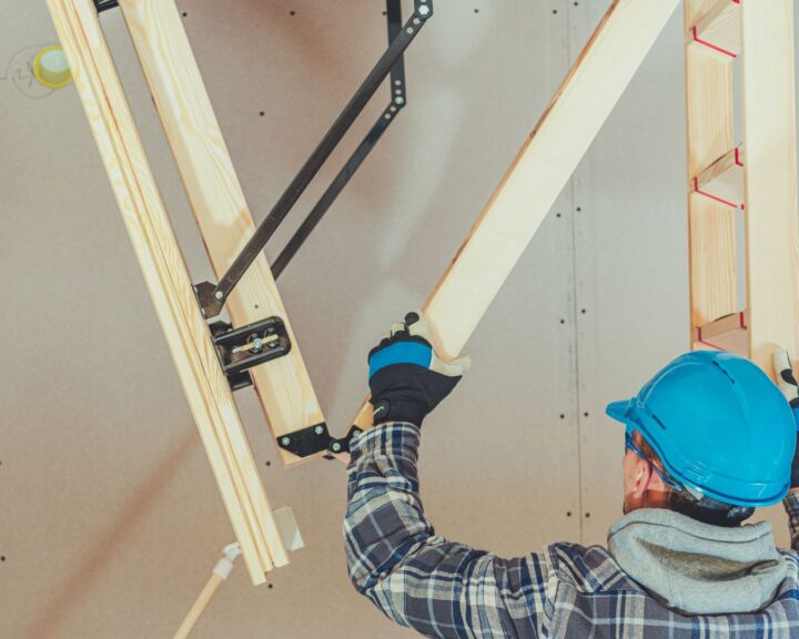 A man is working on a wooden frame in a room, possibly installing loft insulation.